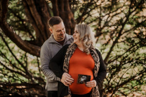 couple hold baby photo in front of pregnancy bump.